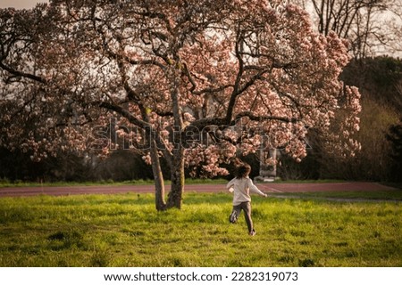 Person in nature. One Asian girl running under blooming Magnolia flowers in sunny day.
