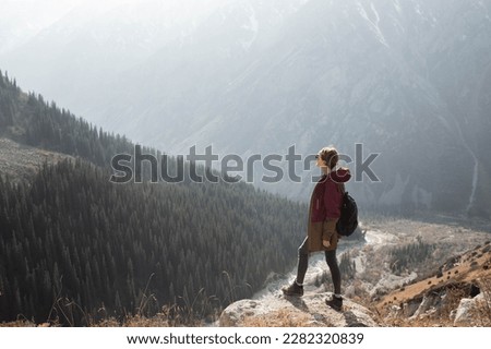 In the photo, a woman is shown standing sideways to the camera, looking out at the mountains. The shot captures her in a full frame. Royalty-Free Stock Photo #2282320839