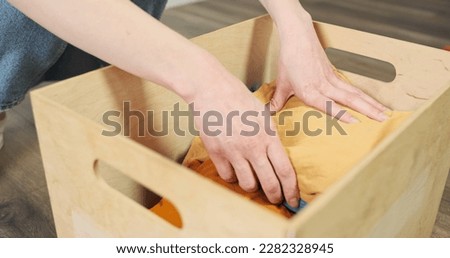 Women's hands put different clothes in box. Side view, indoors. Concept of collecting things for donations, throw away, charity, clean up, housework, storage. Royalty-Free Stock Photo #2282328945