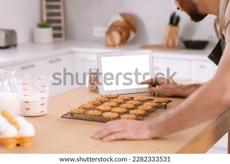 Man with freshly baked cookies watching online cooking course via tablet in kitchen, closeup Royalty-Free Stock Photo #2282333531