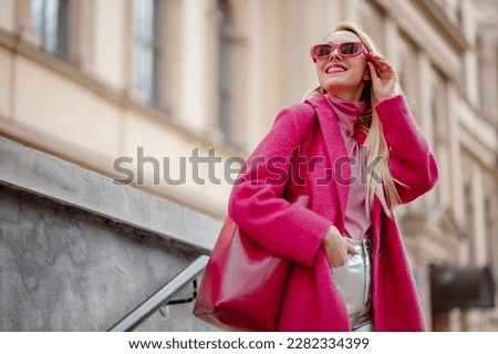 Fashionable happy smiling woman wearing fuchsia color coat, sunglasses, pink turtleneck, holding faux leather tote, shopper bag, posing in street of city. Copy, empty space for text Royalty-Free Stock Photo #2282334399