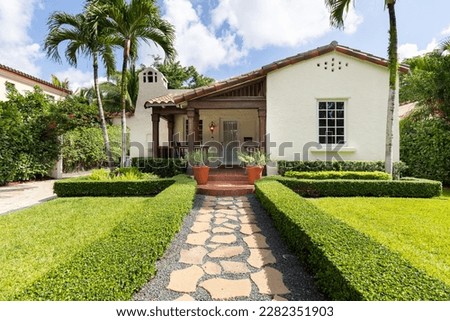 Facade of a colonial-style house with a beautiful front garden, with a path to the main door, driveway, tiled roof, located in the Granada neighborhood in the city of Coral Gables, palm trees and priv Royalty-Free Stock Photo #2282351903
