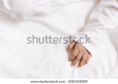 the left hand of a newborn baby wearing a white shirt and mattress with a bright picture