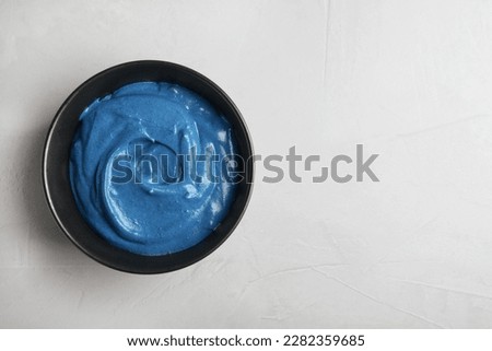 Bowl of cream with blue food coloring on light table, top view. Space for text