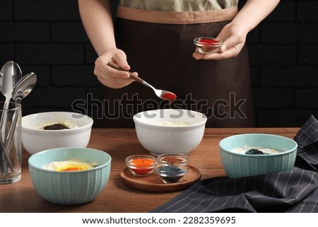 Woman adding red food coloring into bowl at wooden table, closeup