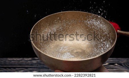 Drops of water fly into the air from hitting a Tibetan (singing) bowl. Cold boil. Tibetan bowl on a black background. High quality photo