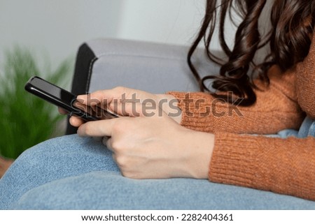 Smartphone in the hands of a woman. Sitting in an armchair. Looks at the display. Internet search, message exchange. Photo closeup