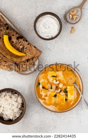 Paneer Butter Masala or Indian Cottage Cheese Curry served in a bowl with rice, fresh vegetables, paratha and cashew nuts. Healthy vegetarian food. Flat lay