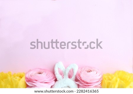 Celebrate the Easter season with this lovely photo featuring fluffy bunny ears, pink flowers, and yellow tulips on a soft pastel background. 