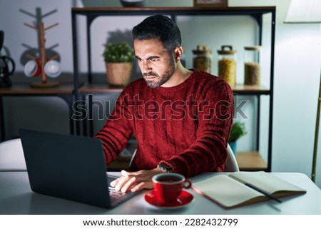 Young hispanic man with beard using computer laptop at night at home skeptic and nervous, frowning upset because of problem. negative person.  Royalty-Free Stock Photo #2282432799
