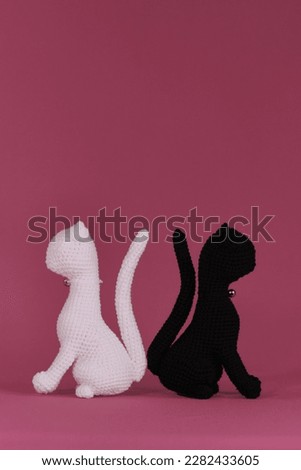 Amigurumi two cats in love sitting on pink background. DIY soft toys made of natural cotton and wool. Crocheted black and white kittens, handmade art. Romantic relationships between pets.