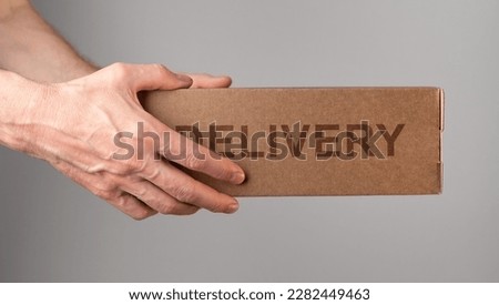Couriers hands holding cardboard box, delivering order, postal parcel in brown package side view.