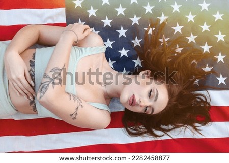 Top view of jewish pretty lady model lying down on american flag, dreaming, closed eyes. Young cute brunette woman with tattoo at flag of USA background. American dream concept. Copy ad text space Royalty-Free Stock Photo #2282458877