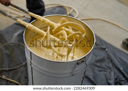 The worker is carefully mixing epoxy composites in a metal bucket to create high-quality polyurethane resin.  Royalty-Free Stock Photo #2282469309
