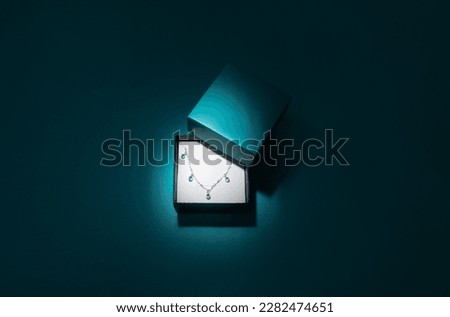 Photography of a silver small bracelet with turquoise gemstones inside a paper jewelry box with no branding and turquoise dark background. Royalty-Free Stock Photo #2282474651