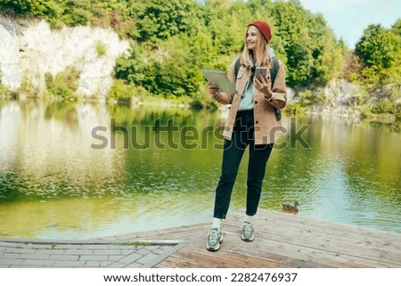 Young lady traveler in a hat near a lake with a paper map and looks into the distance. Mountains and lake on the background. High quality photo