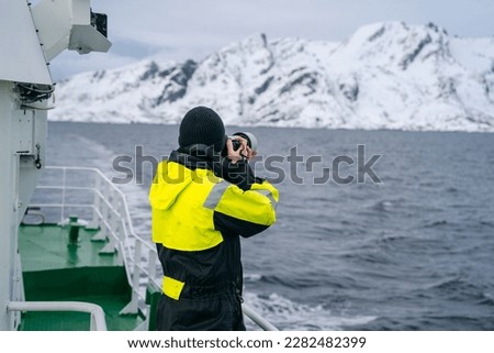 The photographer is dressed in warm clothing, including a hat and gloves. The boat itself is an old, traditional fishing vessel, and appears to be well-worn and weathered by years at sea. Nature photo
