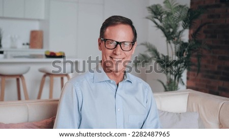 Portrait of smiling happy senior man sit on couch in living room posing for picture at home, cheerful elderly male or grandfather wearing glasses look at camera relaxing on cozy sofa.