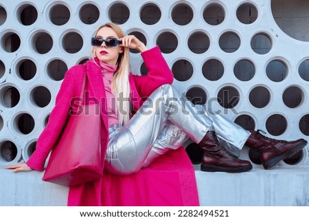 Fashionable confident woman wearing fuchsia color coat, blue sunglasses, pink turtleneck, metallic pants, combat boots, with  faux leather tote bag. Outdoor portrait. Copy, empty space for text Royalty-Free Stock Photo #2282494521