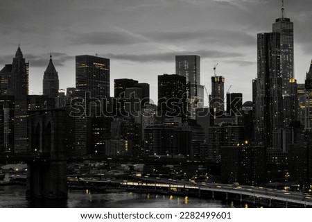 Yellow lights shining in black and white night time cityscape with the Brooklyn Bridge and buildings of Manhattan in New York City NYC