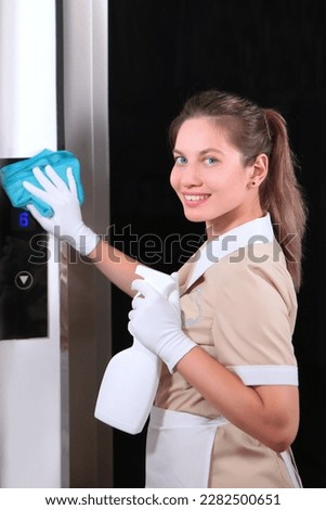 A young girl in a cleaning uniform wipes the glass doors of the Elevator.Concept of cleanliness. Copy space. Vertical photo.