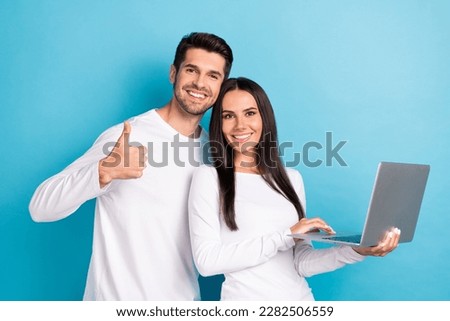 Photo of two cheerful pleasant cute couple people wear white shirts guy show like girl hold laptop isolated on blue color background