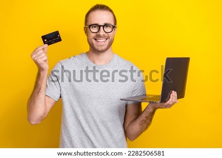 Photo of positive successful man buyer wear trendy clothes demonstrate plastic card modern netbook isolated on yellow color background