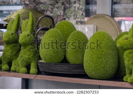 The beautiful moss Easter eggs and playful moss green Easter bunnies on the plates. A large light clay plate, a picture with flowers, a window blurred in the background.