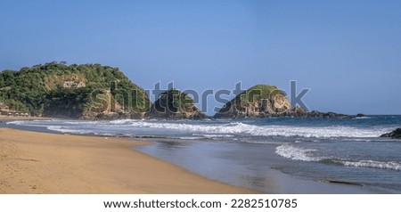 Beach, waves, and hills covered with jungle in the background