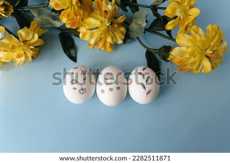 White chicken painted eggs on a blue background and with a bouquet of yellow flowers. Three Easter eggs with a bunny on them. Close up. Free copy space.