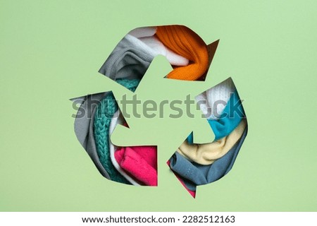Second hand, circular fashion and recycling concept. Colorful clothes under paper cut recycling symbol.