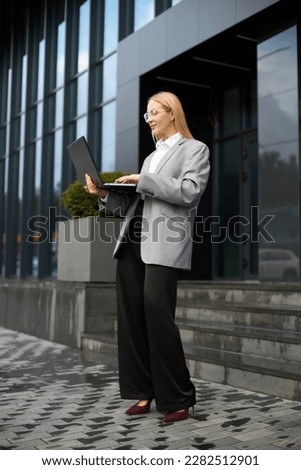 Stylish businesswoman holding laptop checking email, working online using wireless internet connection on the street 