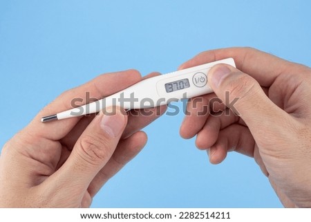 Men's hands hold a digital thermometer on blue background. a person looks at an electronic thermometer with temperature