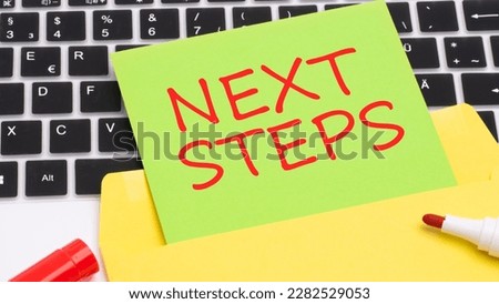 text NEXT STEPS red letters on green and yellow card. in the frame is a laptop keyboard, red marker, white wooden table. concept of business and finance.