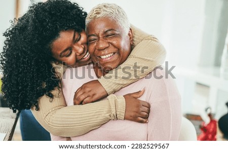 African daughter hugging her mum indoors at home - Main focus on senior mother face - Mom day and family love concept Royalty-Free Stock Photo #2282529567