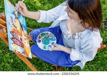 Top view. Young female artist paints picture in summer park in sunlight. Art and hobby concept.