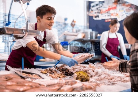 Portrait of salesman offering fresh fish striped red mullet at seafood shop Royalty-Free Stock Photo #2282553327