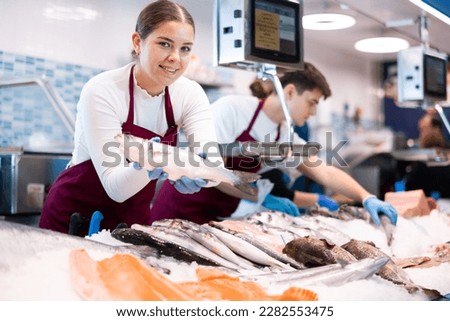 Woman seller of fresh fish advises buyer to buy hake fresh fish Royalty-Free Stock Photo #2282553475