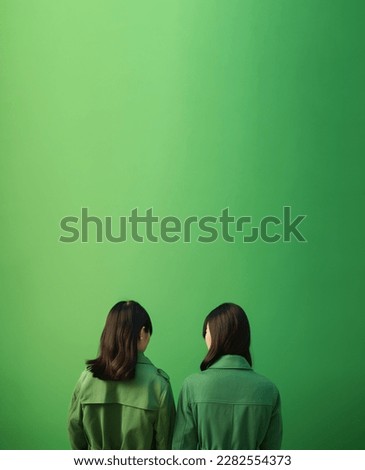 Back view of two asian women with black hair, wearing green clothes, over a green background