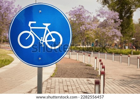 Blue and white traffic sign indicating a bike path or cycle lane at Chapultepec public park in Mexico city with Jacaranda trees blooming on the background marking the beginning of the spring.