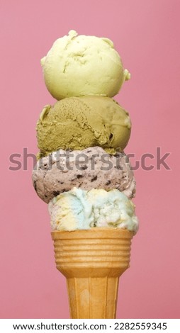 Close-up view of four flavors of ice cream stacked on ice cream cones on pink background.