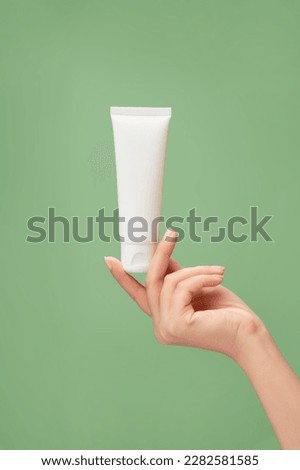Over a pastel green background, woman hand model holding a white tube without label. Beauty product mockup. Natural skincare products concept Royalty-Free Stock Photo #2282581585