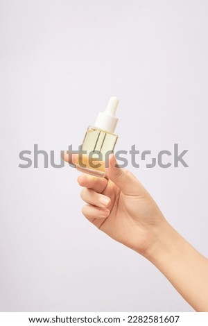 Woman's hand holds mock-up of dropper bottle on white background. Glass bottle without label containing light yellow essence. Space for design, concept of skin care. Royalty-Free Stock Photo #2282581607