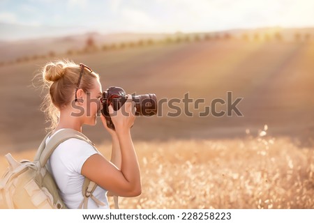 Happy traveler girl photographing ripe wheat field in bright sun rays, autumn harvest season, interesting profession, travel and tourism concept
