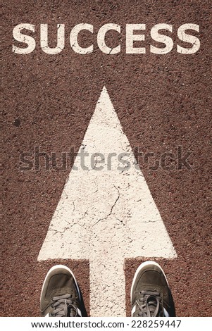 A pair of feet standing on street on white direction arrow. Success concept. Toned photo, low contrast.
