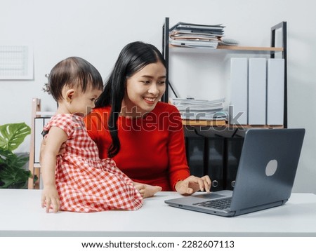 Young business mom asian people woman with baby girl watching video social on laptop computer in the room.