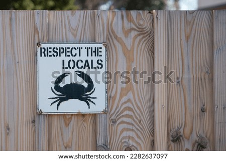 Respect the locals text on wooden fence with icon crab drawing