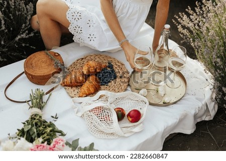 Cropped picture of a woman sitting on a picnic at nature. Concept of having picnic on lavender field at sunset the during summer holidays or weekends.