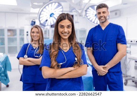 Group of three doctors and nurses standing in a hospital corridor, wearing scrubs. The team of healthcare workers are staring at the camera and smiling