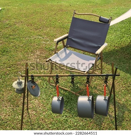 Folding Camping Chair and some Kitchen tools and equipment and pots hanging on the Hanging Pot Stand, camping tent on the green grass field Royalty-Free Stock Photo #2282664511